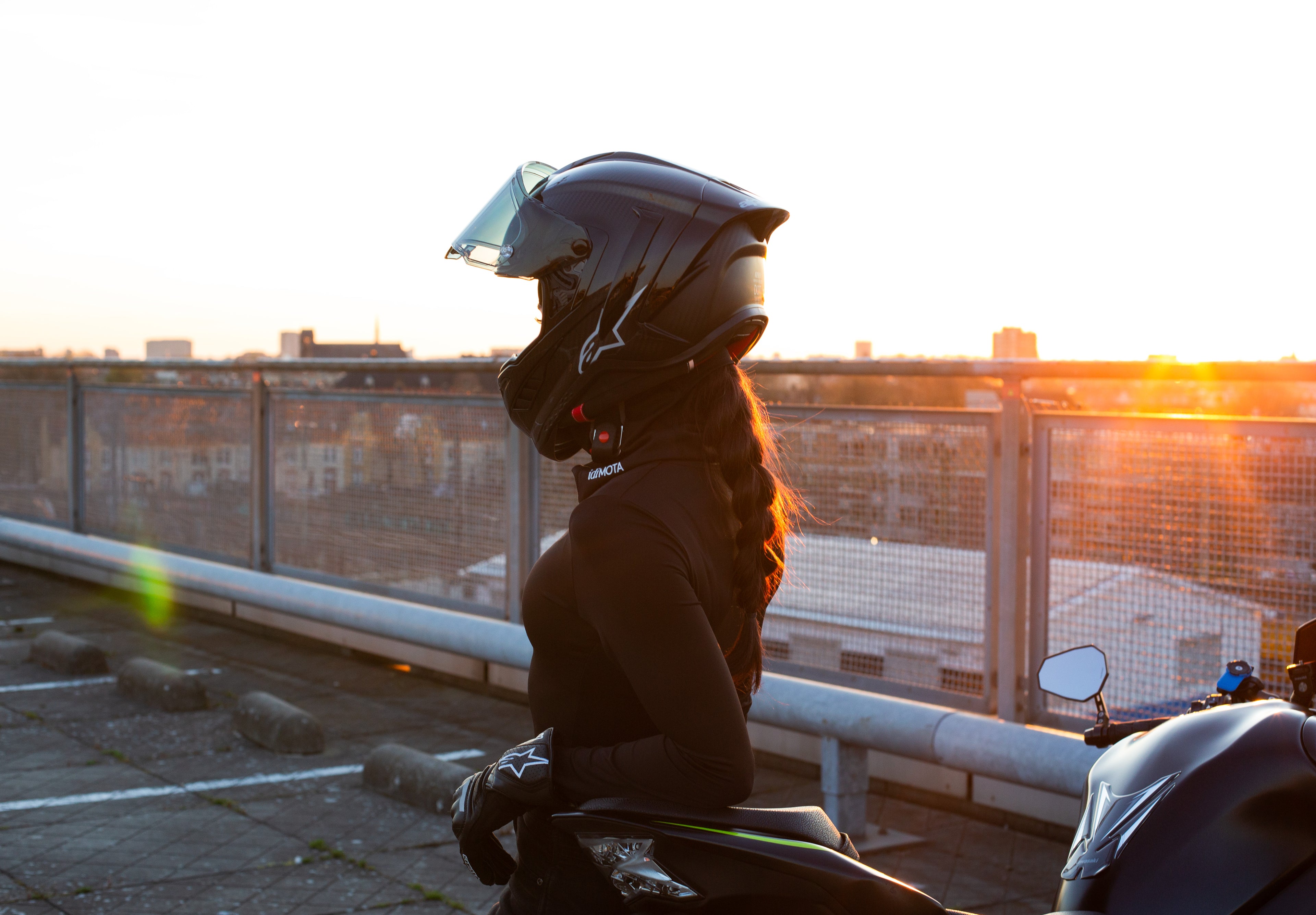 Female rider wearing BRAIDFIT BALACLAVA leaning against motorcycle